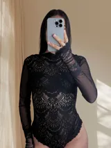 Body de encaje y microtul color negro, con mangas largas, cuello alto y diseño entallado que combina transparencias.