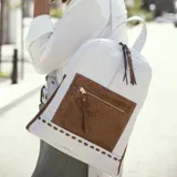 Mochila blanca con textura símil piel de cocodrilo y bolsillo frontal marrón con cierre dorado. Incluye correa extensible para usar como morral.