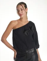 Blusa de un hombro color negro, con diseño asimétrico, una manga larga abullonada, forro interno y apliques de flores de tela en el frente.