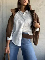 Camisa blanca de corte clásico con sutiles rayas verticales y delicado bordado floral en la parte superior delantera. Presenta cuello camisero, cierre frontal con botones y mangas largas.