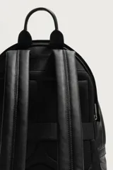 Mochila de diseño minimalista en color negro, confeccionada en material sintético con acabado grabado. Cuenta con un compartimento principal con cierre de cremallera, un bolsillo frontal con cierre y un compartimento posterior acolchado para dispositivos electrónicos. Incluye asa de mano superior y dos correas de hombro ajustables.