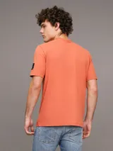 Remera color naranja de corte clásico y manga corta. Tiene cuello redondo y una insignia con el monograma de Calvin Klein en la manga.