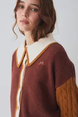 Cardigan de punto multicolor con diseño colorblock, cuello polo rosado con borde rojo, cierre frontal de botones, mangas largas abuchonadas (una roja y otra verde militar con tejido de ochos) y detalles de rayas en los puños y el ruedo.