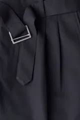 Pantalón sastrero negro de corte relajado, con pinzas frontales, cierre con botón y corchete oculto. Incluye un cinturón extraíble con hebilla metálica. Presenta bolsillos al bies y bolsillos traseros ribeteados.