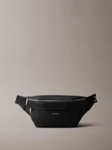 Riñonera Calvin Klein de poliuretano texturizado color negro, con cierre superior de cremallera y un bolsillo frontal con cierre. Cuenta con correa ajustable y detalles metálicos plateados.