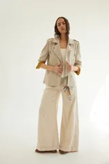 Chaqueta corta de inspiración motoquera color beige, confeccionada en lino fantasía, sin forro, con cierres decorativos, broches de presión y bolsillos delanteros funcionales. Presenta detalle bajo el cuello y en vueltas de mangas en color mostaza y rayas.
