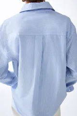 Camisa de corte relajado con diseño a rayas finas en tonos celeste y blanco, cuello clásico, mangas largas con puños anchos abotonados y bajo redondeado.