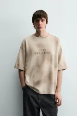Camiseta de punto de algodón con corte relajado (relaxed fit) y cuello redondo. Presenta un estampado frontal con efecto spray en tonos marrones y beige, y un efecto lavado general.