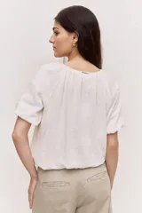 Blusa blanca de manga corta, con escote redondo y cierre frontal con tres botones. Presenta pliegues frontales y diseño liviano.