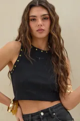 Musculosa crop de morley negro con cuello redondo, decorada con tachas en forma de estrella doradas a lo largo del cuello y sisas. Cuenta con un pequeño bordado frontal en el centro del pecho.