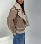 Campera tipo gamulán de color beige, con interior y solapas de corderito sintético en tono crema. Presenta cierre frontal, bolsillos laterales y detalles de costuras reforzadas.