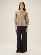 Camisa de lino mezcla color beige, con cuello redondo, cierre frontal con botones y mangas tres cuartos con puños elásticos. Presenta detalles de pespuntes verticales en zigzag en el frente.