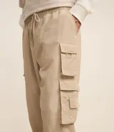Pantalón jogger de poliamida color beige, de corte holgado con cintura elástica ajustable mediante cordón, puños elásticos en los tobillos y cuatro bolsillos cargo laterales con solapa.