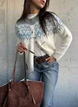 Cardigan de tejido de punto con diseño jacquard en la parte superior, cuello redondo y cierre frontal con botones. Presenta un patrón geométrico en tonos gris y azul sobre base color crema.