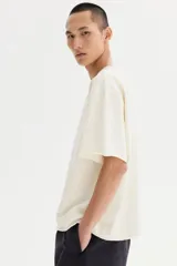 Remera de algodón en punto liviano color beige, con diseño boxy de hombros caídos, cuello redondo con ribete acanalado y corte oversized.