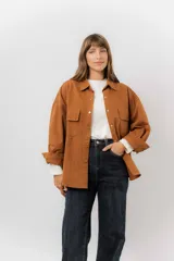 Sobrecamisa de gabardina liviana color crema, con corte oversize, cuello clásico, cierre frontal con botones a presión y dos bolsillos delanteros con solapa.