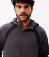 Campera deportiva Get Over de poliéster tecnológico, de color gris oscuro con bandas negras decorativas en los hombros y mangas. Cuenta con capucha ajustable, cierre frontal con cremallera, y puños y cintura elastizados.