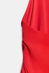 Vestido corto de tejido fluido en color rojo, con cuello halter y diseño asimétrico. Presenta detalles de frunces en el lateral y bajo acabado en volantes con caída irregular.