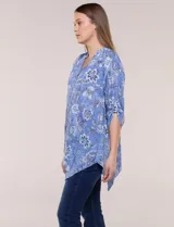 Blusa azul con estampado floral, escote en V, abotonadura frontal y mangas tres cuartos con presilla para arremangar. Cuenta con un diseño amplio y ruedo asimétrico en punta.