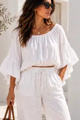 Blusa blanca confeccionada en lino, con escote bote elastizado y mangas acampanadas amplias con volados.