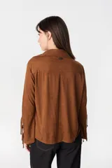 Camisa de manga larga color camel con textura geométrica grabada, cuello clásico y cierre frontal con botones. Presenta un diseño distintivo en las mangas con aberturas laterales y lazos ajustables.