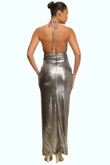 Vestido largo de fiesta en tela metalizada plateada, con cuello halter, detalle de nudo drapeado en la cintura y tajo frontal en la falda.