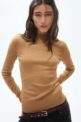 Buzo de punto fino suave color tostado, con diseño entallado, cuello alto acanalado, manga larga y remates acanalados en puños y bajo.