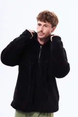 Buzo de sherpa color negro, con cuello alto y cierre frontal parcial. Presenta un diseño de manga larga y textura suave y abrigada.