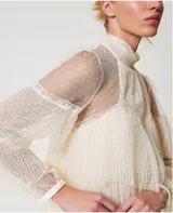 Blusa de tul point d'esprit color marfil, con cuello alto, volantes plisados, inserciones de encaje, mangas largas con puño y botón, cierre de lágrima con botón y placa con el logotipo Oval T en la parte trasera. Incluye top a juego antitransparencia y corte holgado.