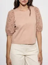 Remera de algodón color rosado con mangas cortas abullonadas de broderie con diseño floral calado. Presenta cuello redondo y costura vertical central en el frente.