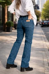 Jean de corte recto y tiro medio, confeccionado en denim azul clásico con costuras en contraste. Presenta un diseño de cinco bolsillos y cierre frontal con botón metálico.