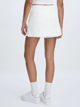 Short pollera blanco de algodón orgánico tejido con cintura con cordón y logo TU bordado en dorado en la parte delantera.