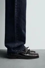 Mocasín de vestir fabricado en piel con acabado brillante, presenta un detalle de lazo en el empeine y suela a contraste con ligero tacón.
