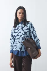 Sweater de punto con diseño estampado de hojas en tonos azul claro y azul oscuro. Presenta cuello redondo, mangas largas y terminaciones acanaladas en puños y ruedo.
