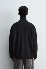 Cárdigan de punto negro con textura de canalé, cuello redondo y cierre frontal de botones.
