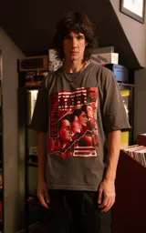 Remera de manga corta con cuello redondo y calce oversize, color gris oscuro. Presenta un estampado frontal con estética retro que incluye figuras humanas y una computadora antigua en tonos rojos.