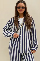 Camisa oversize a rayas verticales azules y blancas, de manga larga con puños abotonados y cierre frontal con botones blancos.