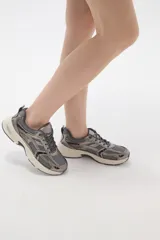 Zapatilla deportiva de estilo urbano en color blanco con detalles metalizados plateados y acentos en negro. Presenta una combinación de malla transpirable y paneles sintéticos, con suela robusta y cordones al tono.