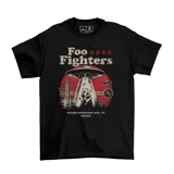 Remera negra de algodón con diseño gráfico frontal de la banda Foo Fighters, que incluye un ovni abduciendo a un carpincho tomando mate frente al Estadio Centenario en Montevideo.