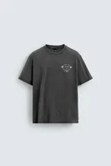 Camiseta de corte relajado con cuello redondo y mangas cortas. Presenta un efecto lavado que le otorga una apariencia única y estampados a contraste en el frente.