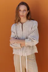 Bomber de tela liviana color beige con textura sutil, cierre frontal completo, mangas largas con puños elásticos y cordón ajustable en el ruedo.