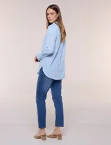 Camisa de calce relajado color celeste, confeccionada en tejido de textura suave y fluida. Presenta cuello camisero y abotonadura frontal, mangas largas con puño ancho y ruedo curvo.