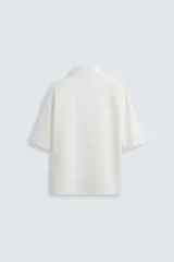 Sobrecamisa negra de tejido con elasticidad, cuello solapa y manga corta. Tiene dos bolsillos de plastrón en el pecho y cierre frontal con botones a presión.