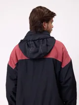 Campera reversible con capucha oculta, confeccionada en sarga de algodón con elastano en el exterior y nylon de poliéster en el interior. Presenta cierre frontal con botones a presión, costuras visibles en contraste y puños elásticos.