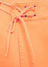 Falda corta de algodón estilo tejano, color naranja, con diseño cruzado y detalle de lazo ajustable con ojales metálicos en la cintura.