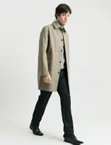 Gabardina clásica de corte recto, color beige, con cuello camisero, cierre frontal de botones y bolsillos laterales. Confeccionada en tejido técnico repelente al agua y al viento.
