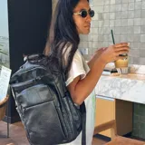 Mochila urbana de cuero sintético negro, con múltiples compartimentos frontales con cierre, bolsillos laterales y compartimento interno para notebook. Cuenta con correas ajustables y diseño funcional para uso diario.