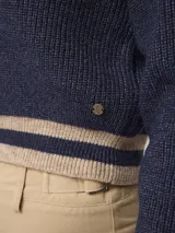 Sweater de punto estilo preppy, color blanco con detalles de rayas negras en el escote en V, puños y ruedo. De corte holgado y manga larga.