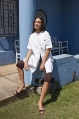 Camisa blanca de corte oversize y largo midi, confeccionada en algodón. Presenta cuello mao, cierre frontal oculto por tapeta y mangas cortas con dobladillo. Incluye un pequeño bordado de una flor en el pecho.