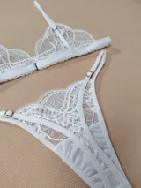 Conjunto de lencería de encaje blanco, compuesto por un corpiño triangular de tirantes regulables y una bombacha tipo colaless con tiras laterales ajustables.